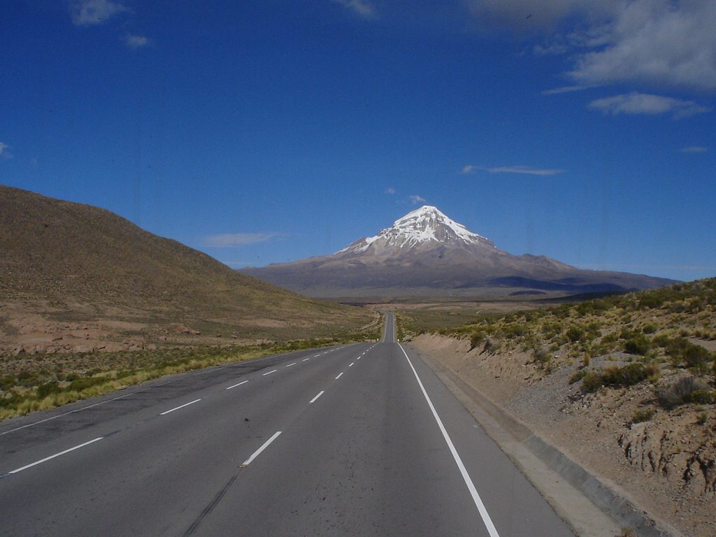 Ruta asfaltada recta hacia un volcán nevado en el altiplano boliviano